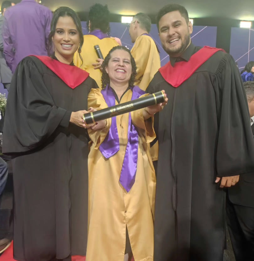 Carla and Daniel in black gowns with Samella in a gold gown, holding her diploma