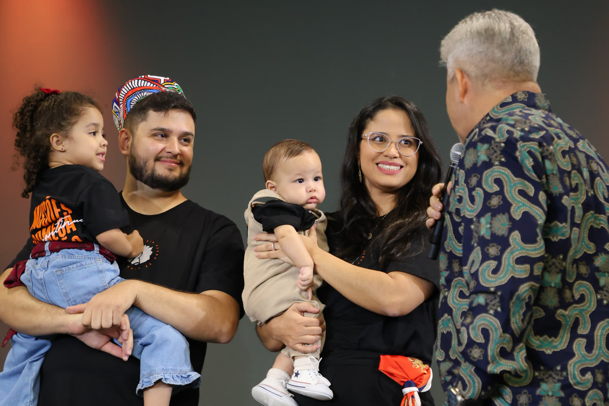 Daniel and Carla on stage holding their children as Pastor Joselito Barbosa speaks to them